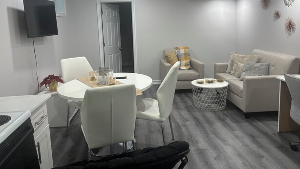 Un salon moderne comprenant un coin repas, un canapé, un téléviseur fixé au mur et une porte donnant sur une autre pièce.