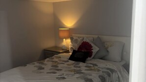 Une chambre à coucher avec un lit, une table de chevet avec une lampe et une bouche d’aération fixée au mur.