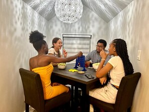 Un coin repas avec une table dressée pour quatre personnes, un lustre et une fenêtre avec des stores.