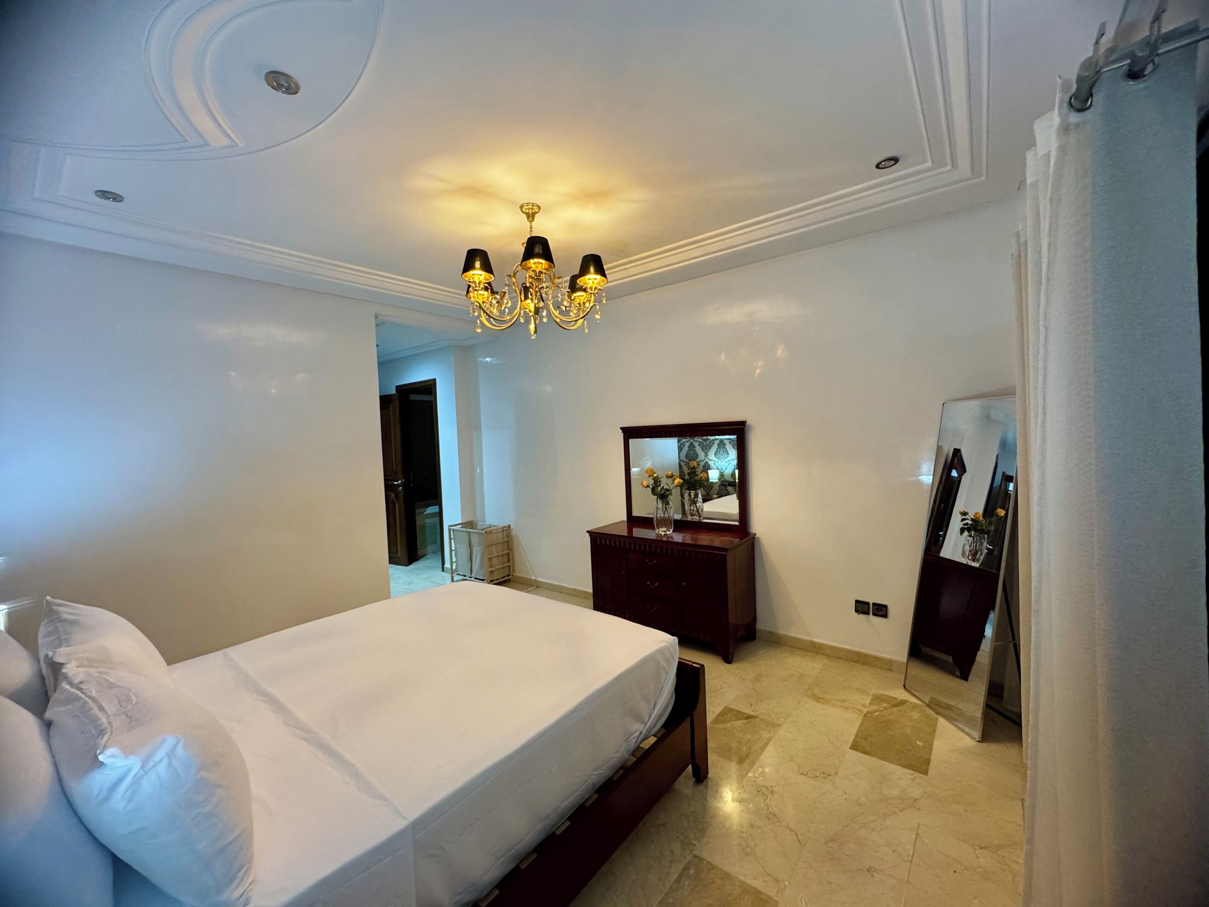 Une chambre à coucher avec un grand lit, une commode, un miroir et un lustre.