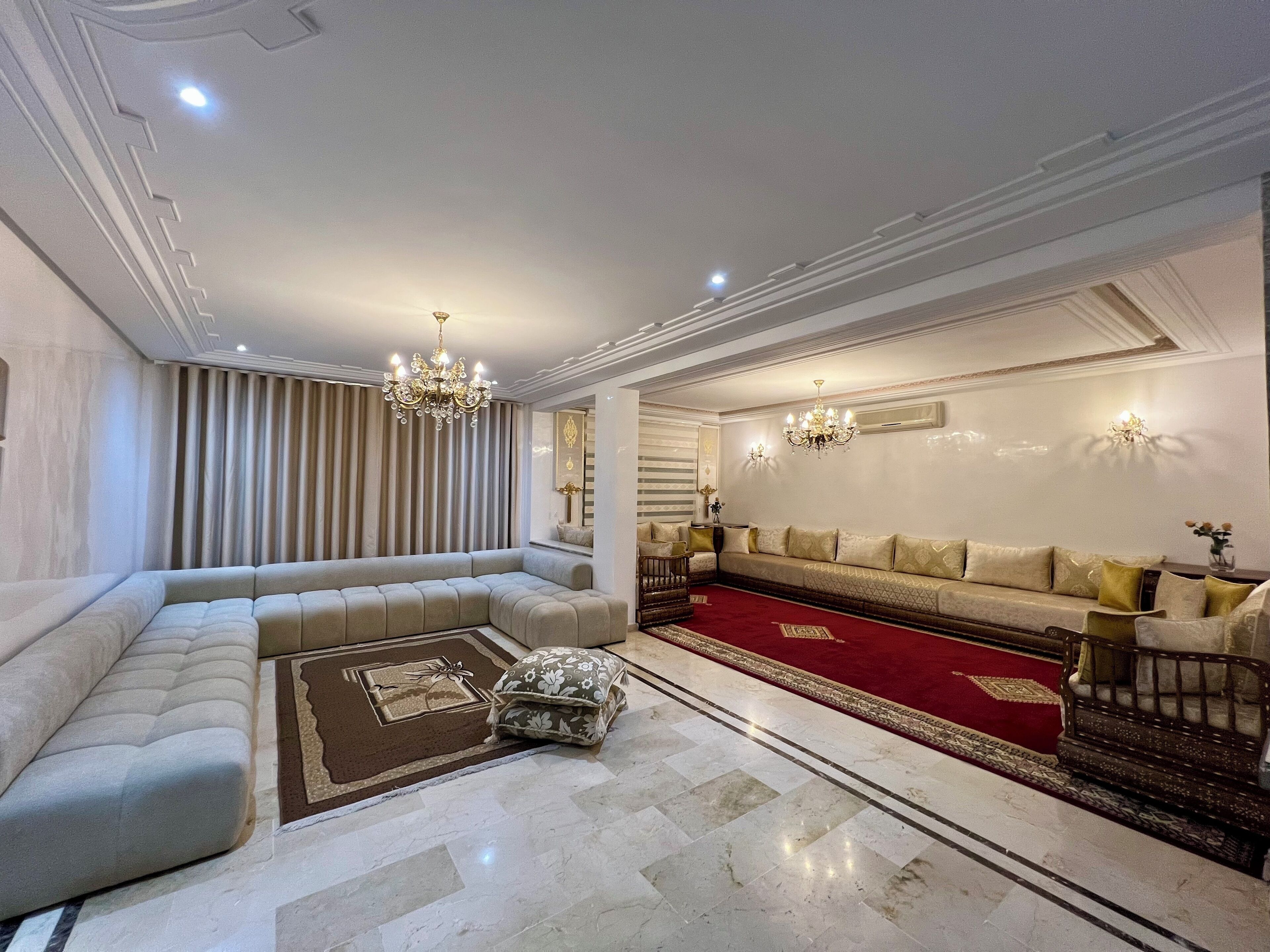 A spacious living room with a large sectional sofa, a red carpet, and a chandelier.