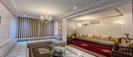 A spacious living room with a large sectional sofa, a red carpet, and a chandelier.