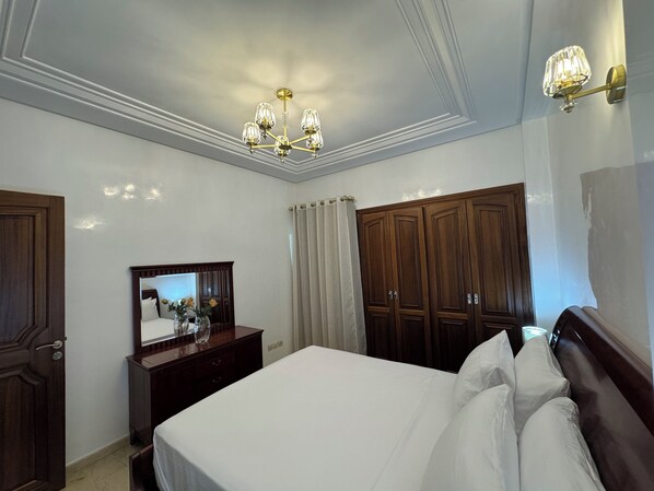 Une chambre d’hôtel avec un grand lit, une armoire en bois, une commode, un miroir et un lustre.