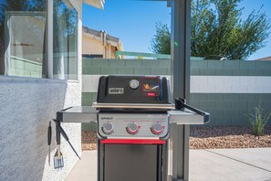 A Weber Spirit grill with a digital display and control knobs, positioned outdoors with a clear view of the sky and a building in the background. - Stylish 4BR Oasis w/ Pool, Spa, Firepit, Ping Pong (North Las Vegas)