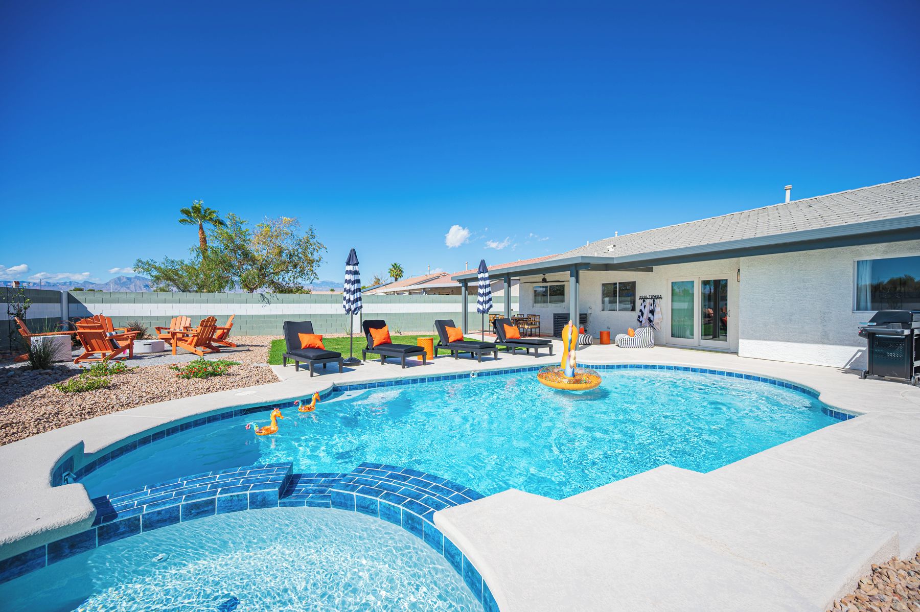 A swimming pool with lounge chairs and umbrellas, a covered patio area, and a view of mountains in the background.