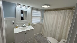 Ein Badezimmer mit Waschbecken, Spiegel und Toilette. Es gibt ein Fenster mit Jalousien und eine Duschvorhang.