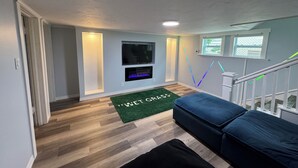 Ein modernes Wohnzimmer mit Flachbildfernseher, Kamin, grünem Teppich und blauem Sofa.