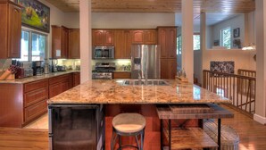 A spacious kitchen with wooden cabinets, granite countertops, stainless steel appliances, and a large island with stools. - Palisades-Alpine Home w/ Hot Tub (Alpine Meadows)