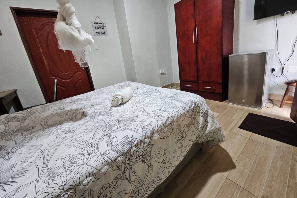 A bedroom with a bed, a wardrobe, a television, and a small table.