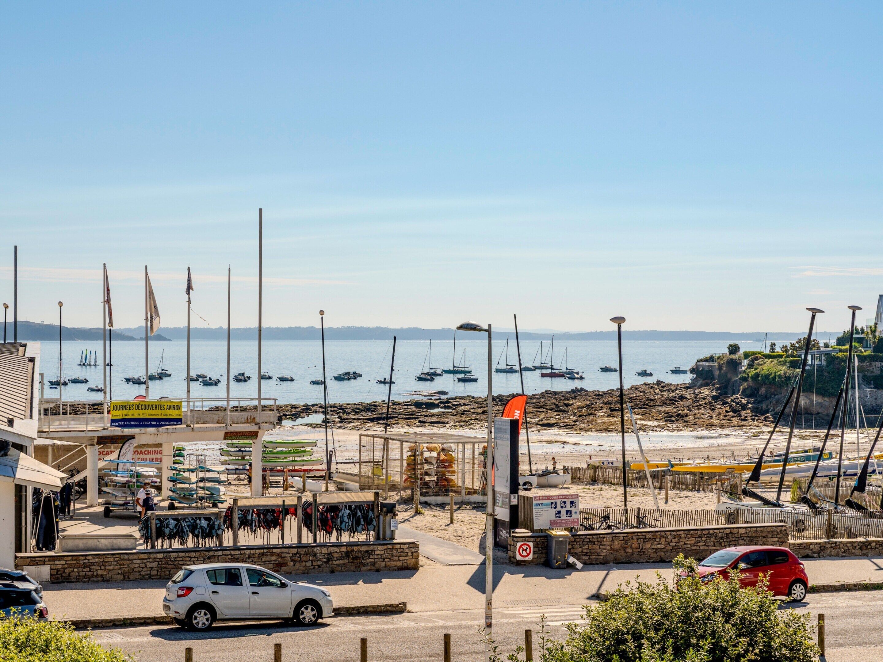 Un port de plaisance sur la côte, avec des bateaux, une voiture et un bâtiment portant une enseigne.
