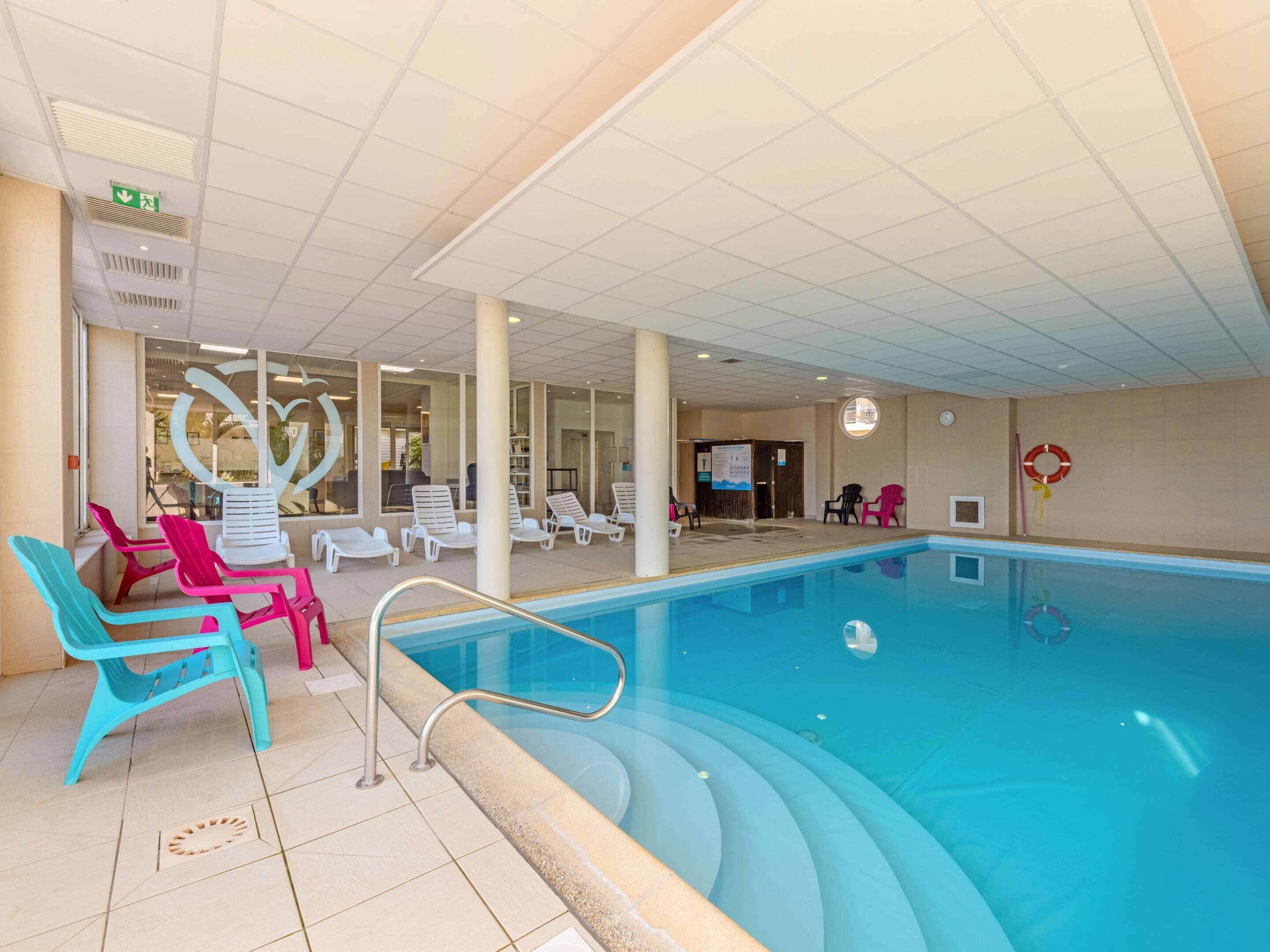 An indoor swimming pool with lounge chairs and a clear ceiling.