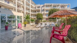 Un hotel moderno con zona de piscina en la azotea, con tumbonas y un parasol de paja.