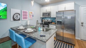 A modern kitchen with white cabinets, stainless steel appliances, a granite countertop, and blue bar stools. - OTR by TQL+Smart TVs+King Bed+Wifi+Sleeps 3+1st Fl (Cincinnati)