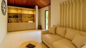 A modern living room with a beige sofa, a wooden coffee table, and a built-in shelving unit with kitchen appliances. - TULUM Koh Samui (Koh Samui)