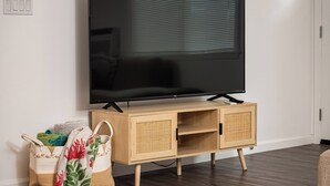 A flat-screen TV mounted on a wall, a wooden cabinet with a woven front panel, and a woven bag with a floral pattern.