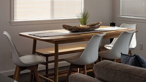 A dining area with a wooden table, white chairs, and a woven basket with a plant.
