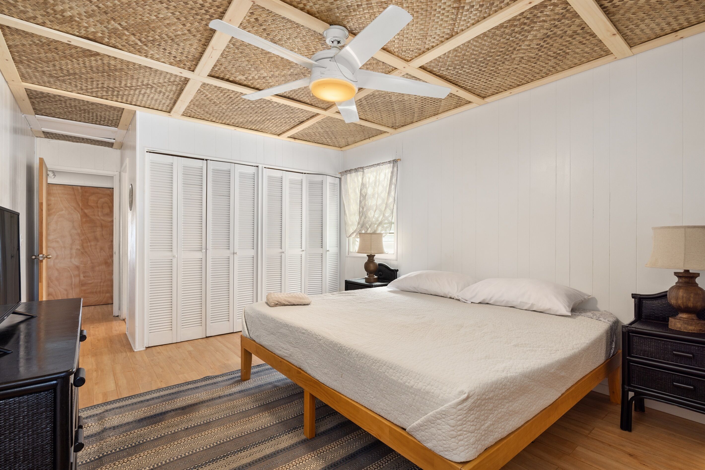 Ein Schlafzimmer mit Bett, Deckenventilator, Nachttisch, Lampe und einer Tür zu einem Schrank.