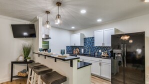 A modern kitchen with a black refrigerator, white cabinets, a blue tiled backsplash, and a bar area with stools. - Tulsa Expo Modern Chic Stay - 1.5 mi to expo (Tulsa)