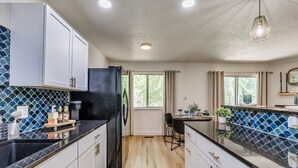 A modern kitchen with white cabinets, a black refrigerator, and a blue-tiled backsplash. - Tulsa Expo Modern Chic Stay - 1.5 mi to expo (Tulsa)