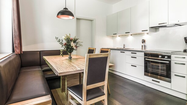 Une cuisine moderne avec des meubles blancs, un four encastré et un coin repas comprenant une table et des chaises en bois.