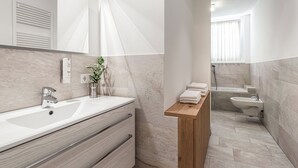 Une salle de bain moderne avec un grand lavabo, un miroir, une étagère en bois avec des serviettes et des toilettes séparées.