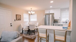 A modern kitchen with white cabinetry, a central island, and a dining area with white chairs. - The Central Nest-3bd/1bth -2.5miles from Casino (Danville)