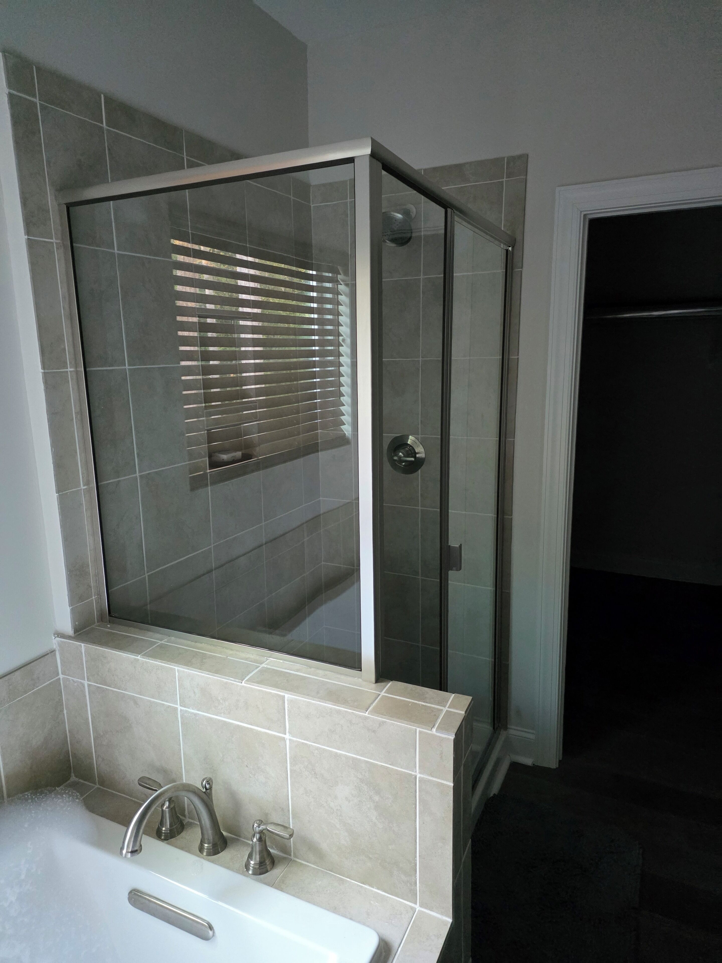 Ein Badezimmer mit einer Glaskabine zur Dusche, einem Waschbecken mit zwei Wasserhähnen und gefliesten Wänden.