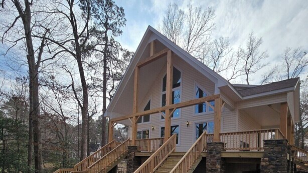 A two-story log cabin with a stone foundation, wooden staircase, and a covered porch area.