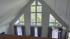 A room with a sloped ceiling, large windows, and a wooden beam.