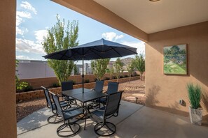 An outdoor patio with a table and chairs, a large umbrella, and a potted plant. - Spacious Family Friendly 5BR Retreat Sandia Views Movie Lounge + Fenced Yard (Albuquerque)