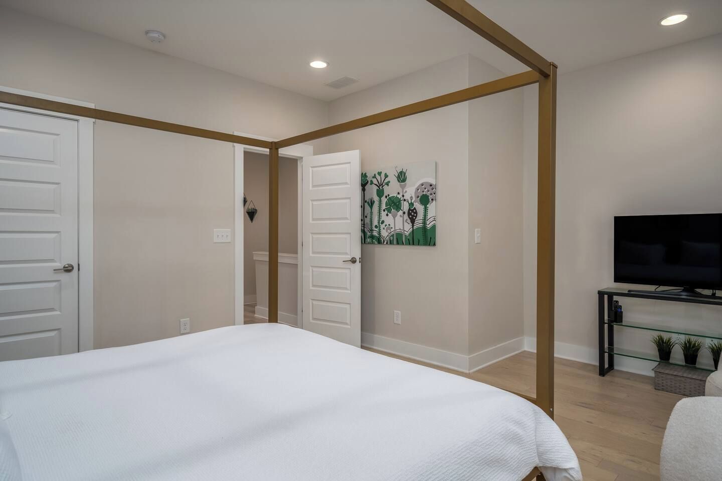 A bedroom with a bed, a television on a stand, and a door leading to another room.