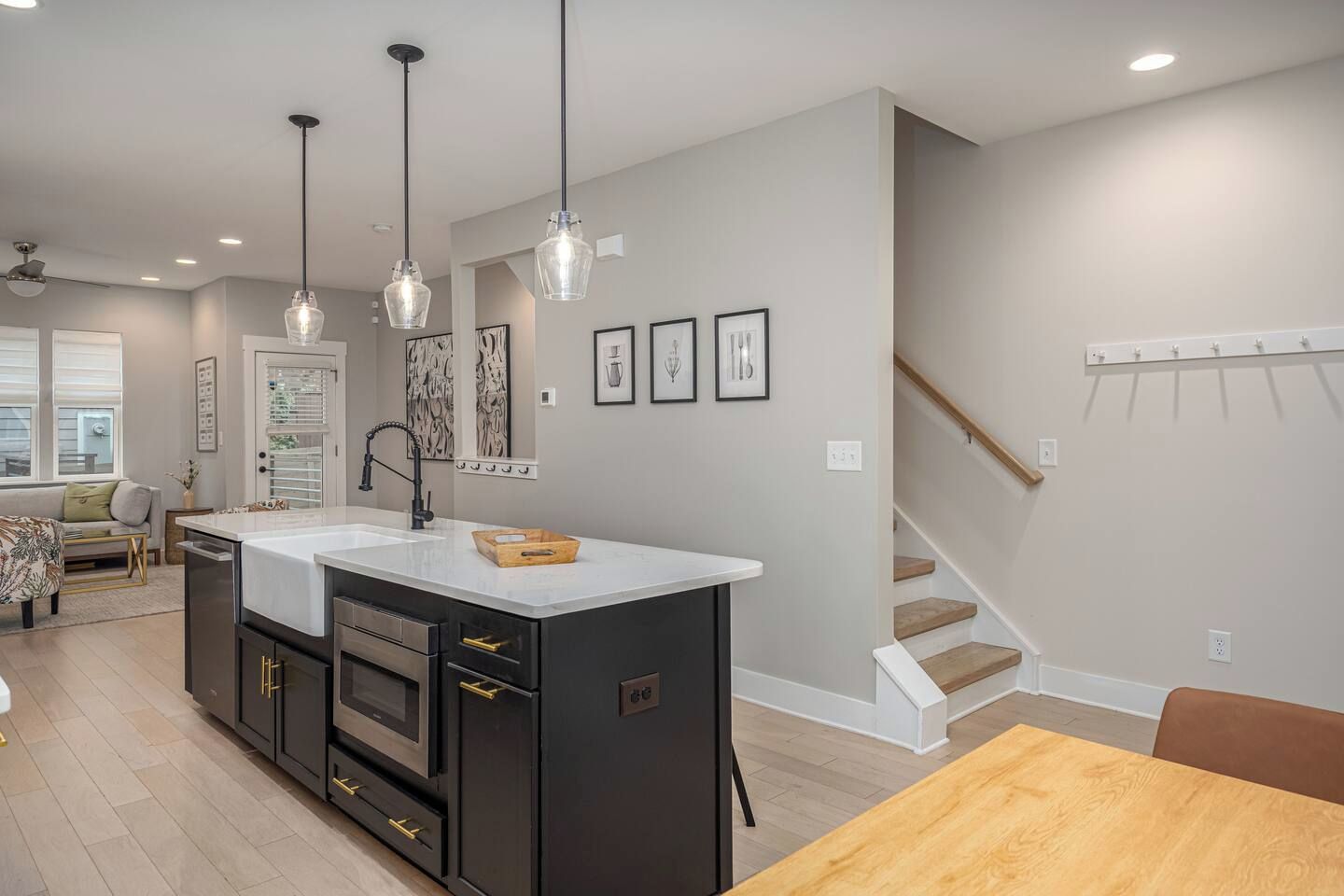 A modern kitchen with a central island, pendant lighting, and a staircase leading to another level.