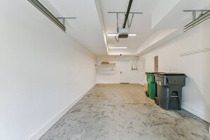 A hallway with white walls, a marble floor, and a door at the end. There are two trash bins and a shelf on the wall.