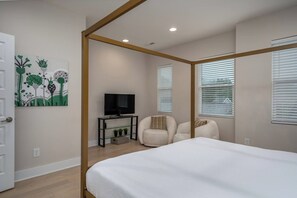 A bedroom with a four-poster bed, a television on a stand, a chair, and a painting on the wall.
