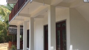 A modern two-story house with a covered porch, large windows, and a thatched-roof structure in the background. - Sun Ray Beach Villa (Kahandamodara)