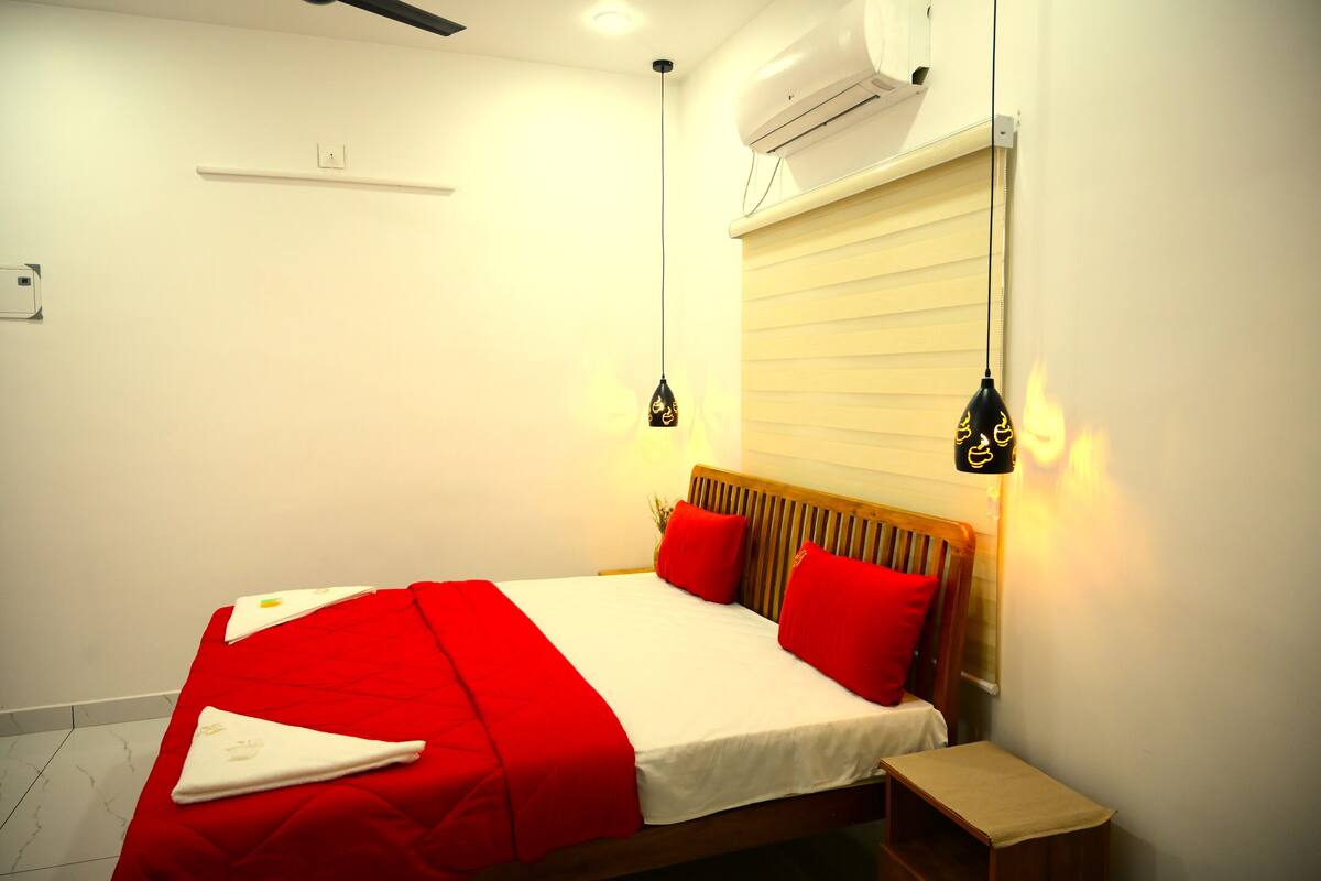 A neatly made bed with red and white bedding, a bedside table, and two pendant lights.