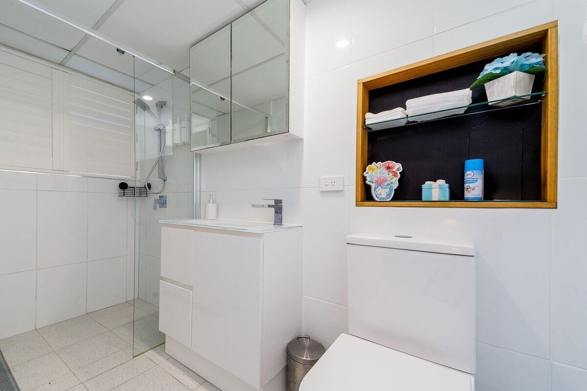 Un baño moderno con cabina de ducha de vidrio, un lavabo blanco y un estante con artículos de aseo.