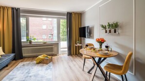 A modern living room with a sofa, a dining table with chairs, a TV mounted on the wall, and a window with curtains. - Fewo7Home New opening apartment at the university (Oldenburg)