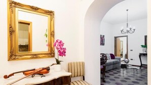 Ein Wohnzimmer mit einem großen Spiegel, einer Violine, einer Orchidee im Topf und einem gemusterten Sessel.