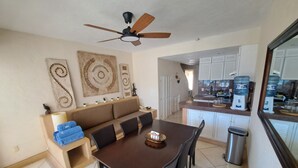A dining area with a brown table, black chairs, and a ceiling fan. There are decorative wall art pieces and a kitchen area visible in the background. - Apartamento familiar con vista espectacular al mar (Ixtapa)