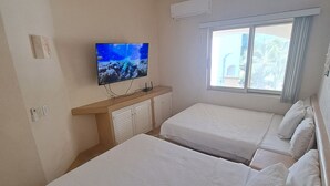 A hotel room with two beds, a television, and a window with a view of palm trees. - Apartamento familiar con vista espectacular al mar (Ixtapa)