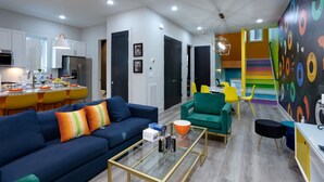 A modern living room with a blue sofa, a glass coffee table, and a colorful wall mural. - Sweet Beat by ES ★ 4/4 ★ 13 Beds ★ Rooftop ★ HUGE (Nashville)