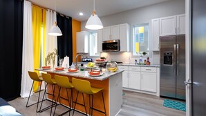 A modern kitchen with white cabinets, a stainless steel refrigerator, a central island with bar stools, and a hanging pendant light. - Sweet Beat by ES ★ 4/4 ★ 13 Beds ★ Rooftop ★ HUGE (Nashville)