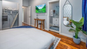 Une chambre avec un lit, une télévision, une salle de bain avec un miroir et une plante.