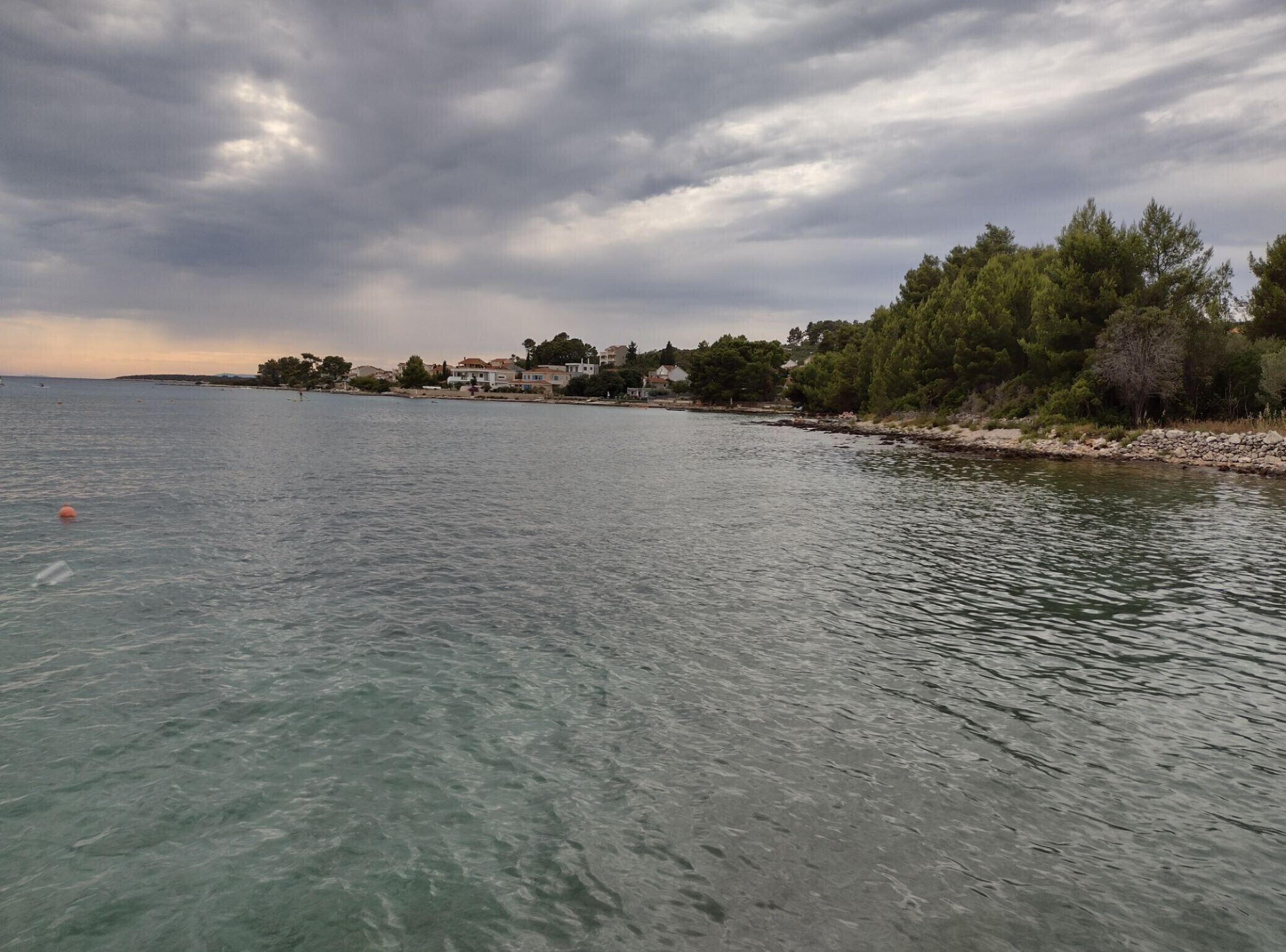 Vista costera con un mar tranquilo, una costa rocosa y edificios a lo largo de la costa.