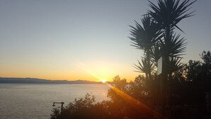 A sunset view over a body of water with a palm tree and a chair in the foreground.