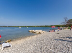 A pebbled beach with clear water, a few people, and a sailboat in the distance. - Apartment Brioni - Two Bedroom Apartment with Terrace (Porec)