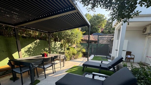 Un patio al aire libre con una mesa y sillas, sillones de descanso y una pérgola.