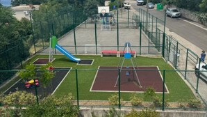 Un patio de juegos cercado con tobogán, columpios y cancha de baloncesto.