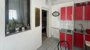 A compact kitchen with red cabinets, a sink, and a window with a view of the outside. - Duga House Apartment A2 (Crikvenica)